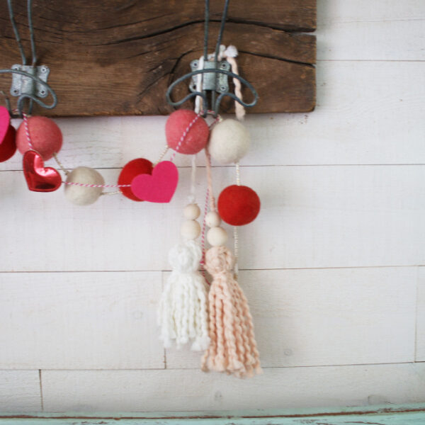 Such a cute yarn home decor neutral tassel for Valentine's Day! Love this pretty soft pink yarn tassel, the cutest Valentine's Day garland! #vintagevalentinesday #valentinesdaydecor #vdaydecor #vdaymantel #valentinesdaymantel #bluemasonjarcollection #pinkvaletinesdaydecor #pinkyarntassel #woodbeadtassel #valentinesdaygarland